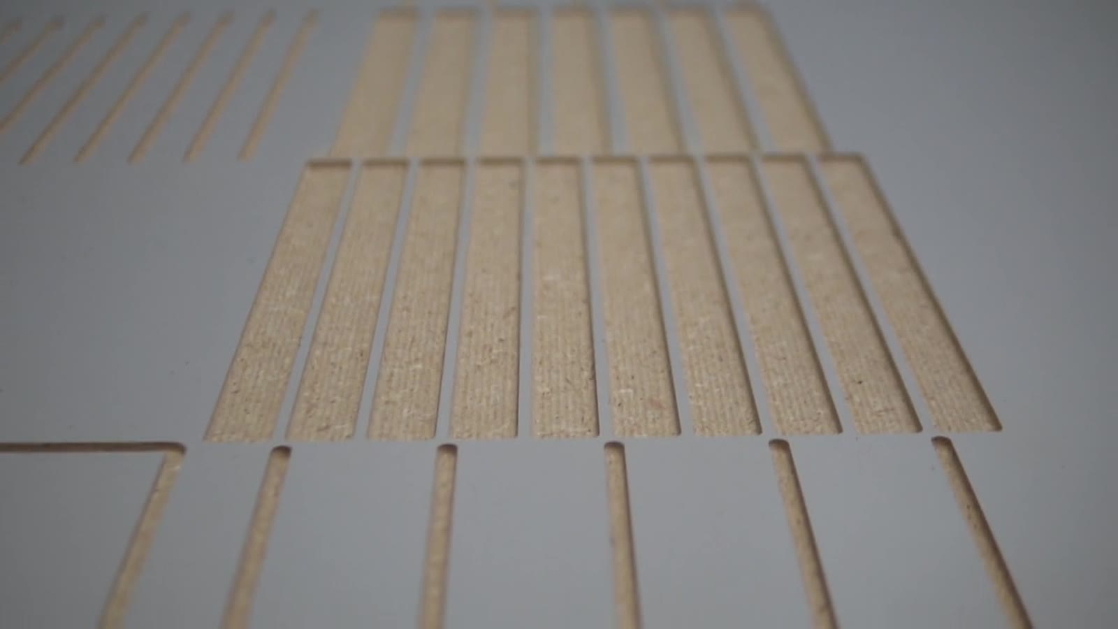 Slotted panel sample with rows of straight slots cut through a grey-faced sheet