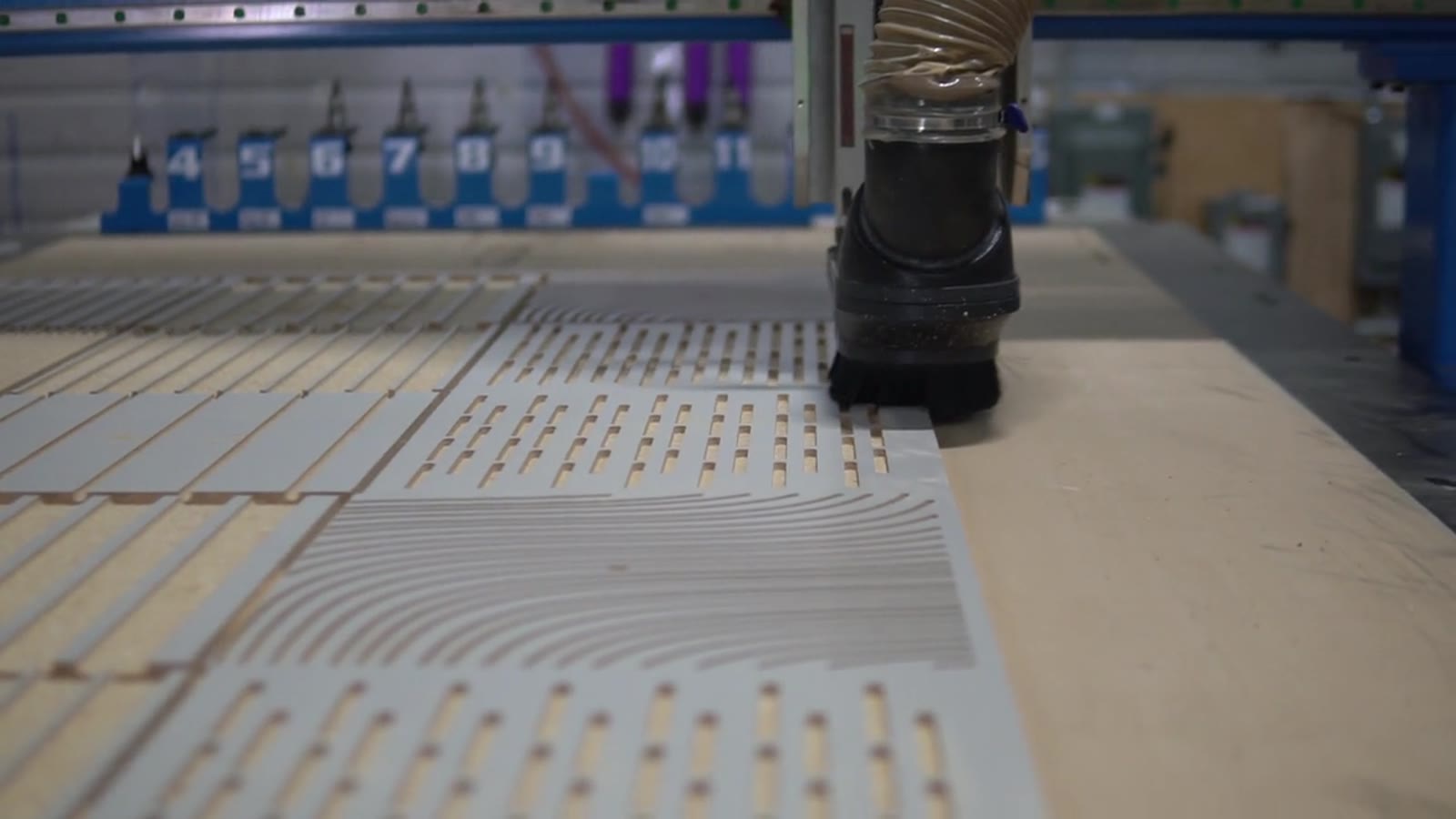 A grid of sample tiles with different groove patterns on the CNC table, the spindle above them
