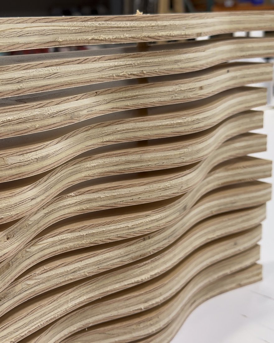 Close-up of our first wave panel: a stack of wavy slats cut from sheet stock, side-lit on the shop bench